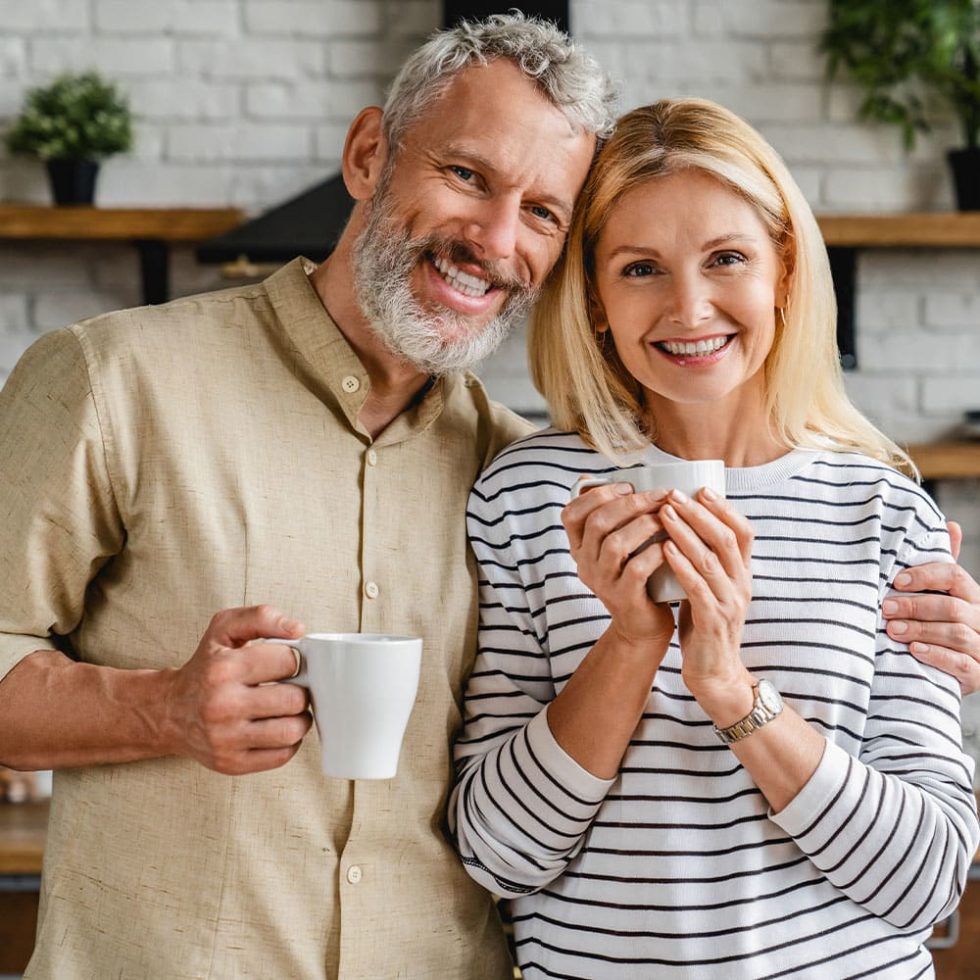 Beautiful couple bonding and smiling while sitting in the kitchen and holding a cup of tea.
